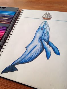 a drawing of a blue whale with a boat in the background on a wooden table