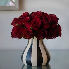 a black and white striped vase filled with red roses