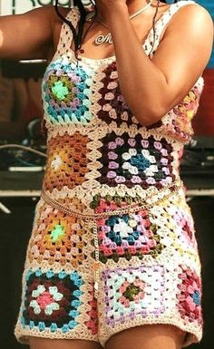 a woman in a crocheted dress holding a cell phone to her ear and singing into a microphone