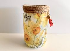 a jar that has flowers on it with a rope in the bottom and a red tassel