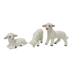 three white sheep standing next to each other on top of a white surface with one laying down