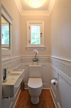 a white toilet sitting under a window next to a sink and mirror in a bathroom