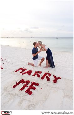 a man and woman kissing on the beach with letters spelling happy new year written in sand