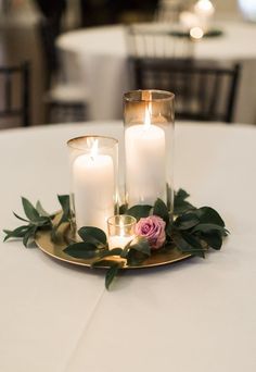 three candles are sitting on top of a plate with greenery and roses in it