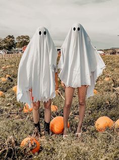 two people dressed up as ghost standing in a field with pumpkins