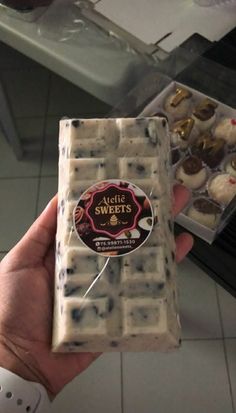 a person holding up a box of cookies in front of some other boxes on the counter