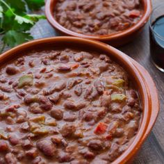 two bowls filled with beans and vegetables on top of a wooden table