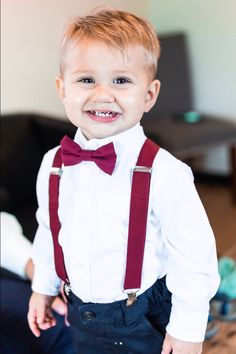 a young boy wearing a red bow tie and suspenders smiles at the camera with his hands in his pockets