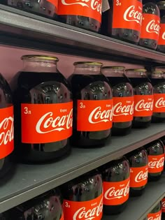 coca - cola bottles are lined up on shelves in a grocery store, with red labels