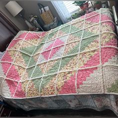 a bed with a pink and green quilt on it's coverlet next to a window