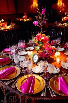 the table is set with pink and yellow plates, silverware, and flowers in vases