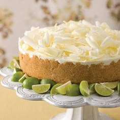 a cake with limes and white frosting on a silver platter next to a floral wallpaper