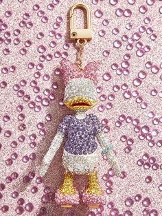 a keychain that has a stuffed animal in it's hand on a pink and purple sequin background