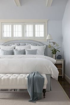 a white bed sitting in a bedroom next to a window with shutters on it