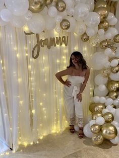 a woman standing in front of a backdrop with white balloons and gold foiled letters