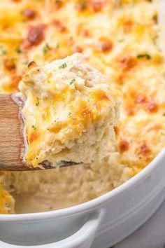 a wooden spoon scooping out some cheesy potatoes from a casserole dish