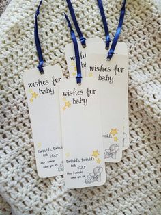 three baby shower bookmarks with blue ribbon on them sitting on a white crocheted blanket