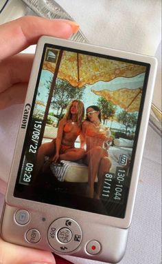 a person holding up a cell phone with two women on the screen and an umbrella in the background