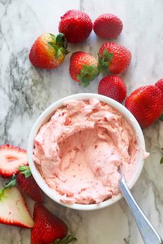 a white bowl filled with strawberry cream next to sliced strawberries on a marble counter