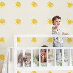 two young children standing on top of a white crib next to a wall with yellow sun decals