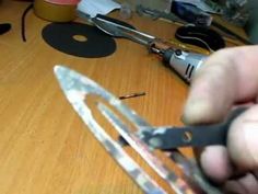 a person holding a pair of scissors on top of a wooden table next to other tools