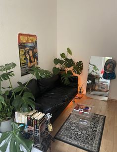 a living room filled with lots of plants and books on the floor next to a black couch