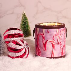 a pink tin with candy canes and a small christmas tree in the snow next to it