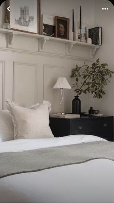 a bed with white sheets and pillows next to a wall shelf filled with pictures on top of it