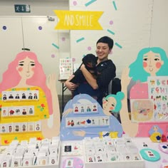 a woman holding a dog in front of a table full of greeting cards and magnets