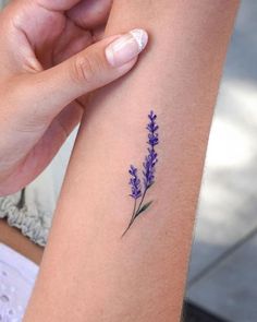 a woman's arm with a small purple flower tattoo on the left side of her arm