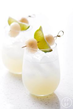 two glasses filled with drinks and garnished with limes on the rim, sitting on a white surface