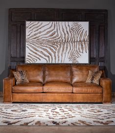 a brown leather couch sitting in front of a large painting on the wall above it