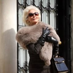 an older woman with white hair wearing black leather gloves and a fur stole around her shoulders