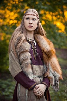 a woman with long hair wearing a fur stoler and standing in front of trees