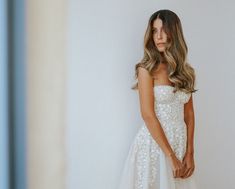 a beautiful woman in a white dress posing for the camera with her hand on her hip