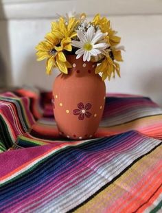 there is a vase with flowers in it sitting on a striped blanket, next to a window