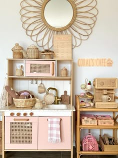 a pink and white kitchen with baskets on the shelves, an oval mirror above it