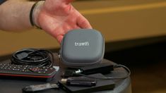 a person holding a remote control on top of a table next to other electronic devices