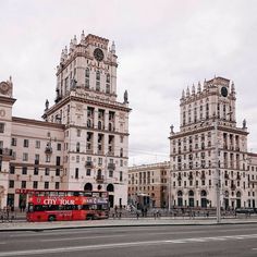 two red double decker buses parked in front of tall buildings with clocks on the top