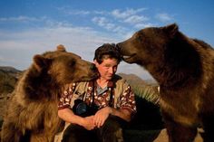 a man kneeling down next to two brown bears