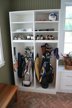 a white bookcase filled with lots of golf bags and equipment next to a window