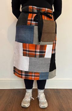 a woman standing in front of a wall wearing an orange and black patchwork apron