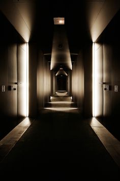 an empty hallway with lights shining down on the floor and walls, leading to two elevators