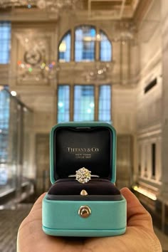 a person holding an engagement ring in a blue box with the words tiffany & co on it