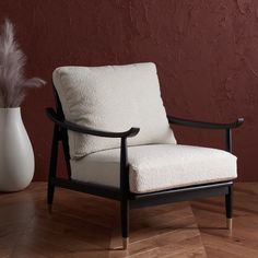 a white chair sitting on top of a wooden floor next to a vase filled with feathers