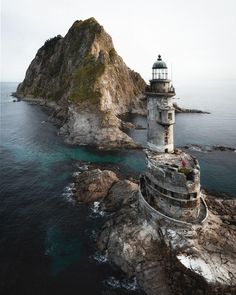 an aerial view of a lighthouse on top of a rocky outcropping in the ocean