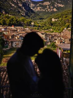 the shadow of two people standing in front of a mountain town with houses and mountains behind them