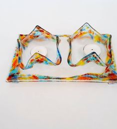 two glass candlestick holders sitting on top of a white surface with multicolored designs