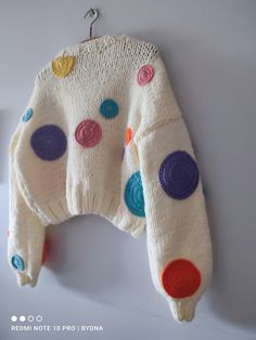 a white sweater with multicolored polka dots hanging from a hook on a wall