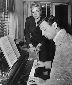 an old black and white photo of a man playing the piano with a woman looking on